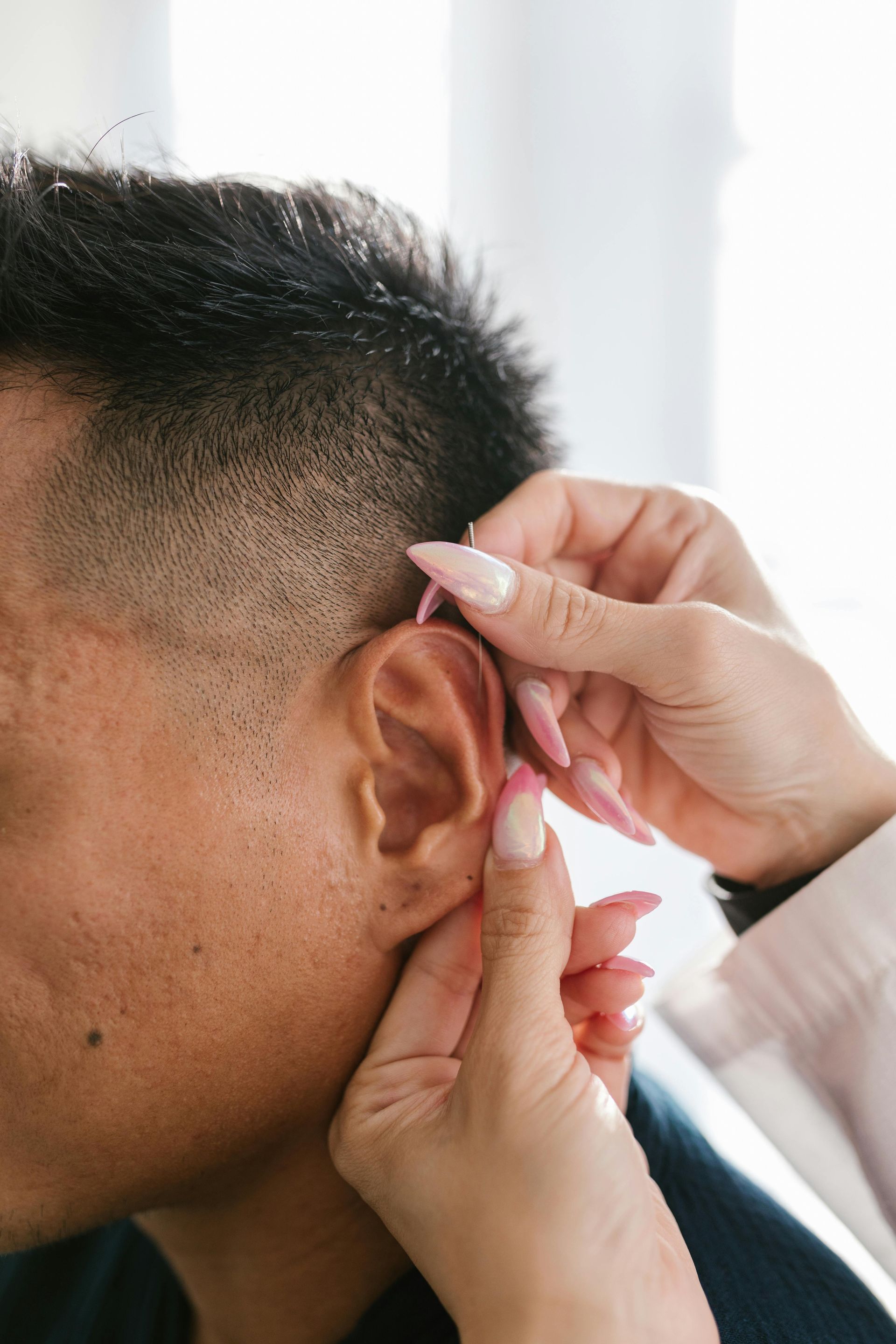 Hands adjusting an ear on a person with a short fade haircut