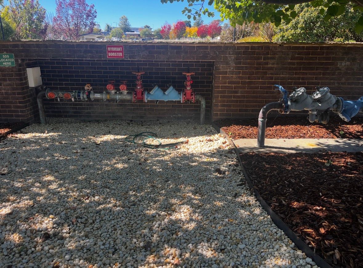 Outdoor garden fountain with animal sculptures against a brick wall, surrounded by gravel and mulch. — T. Woods Plumbing in Bathurst, NSW