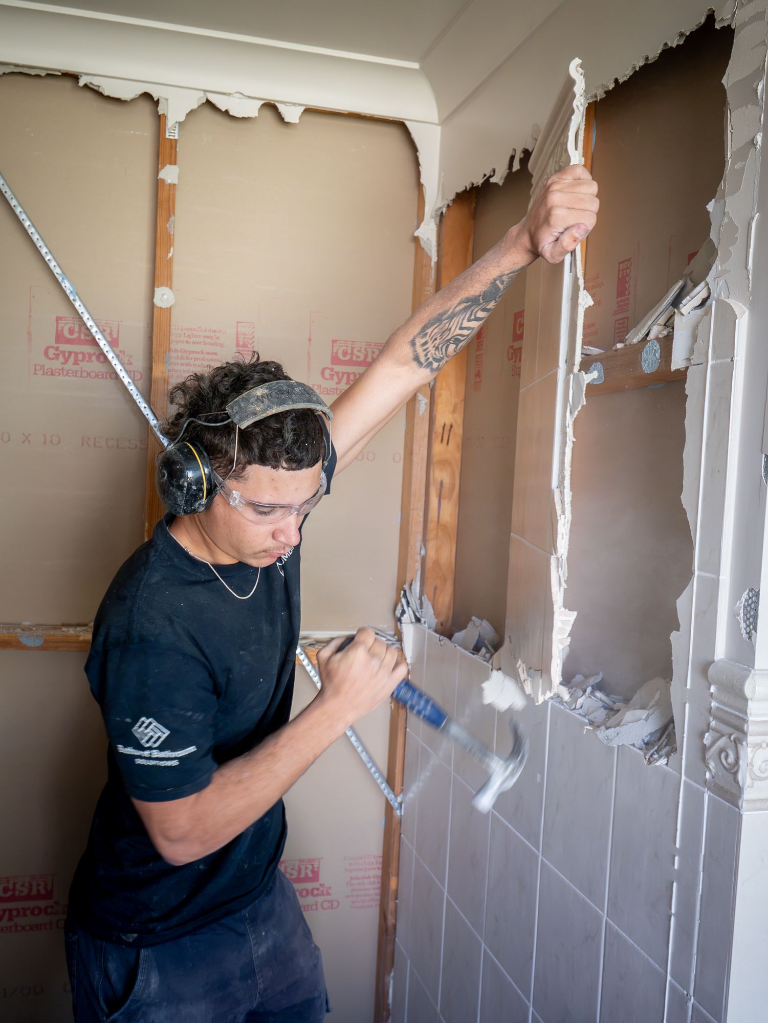 Person demolishing a tiled wall with a hammer in a small room, debris falling around them. — T. Woods Plumbing in Bathurst, NSW