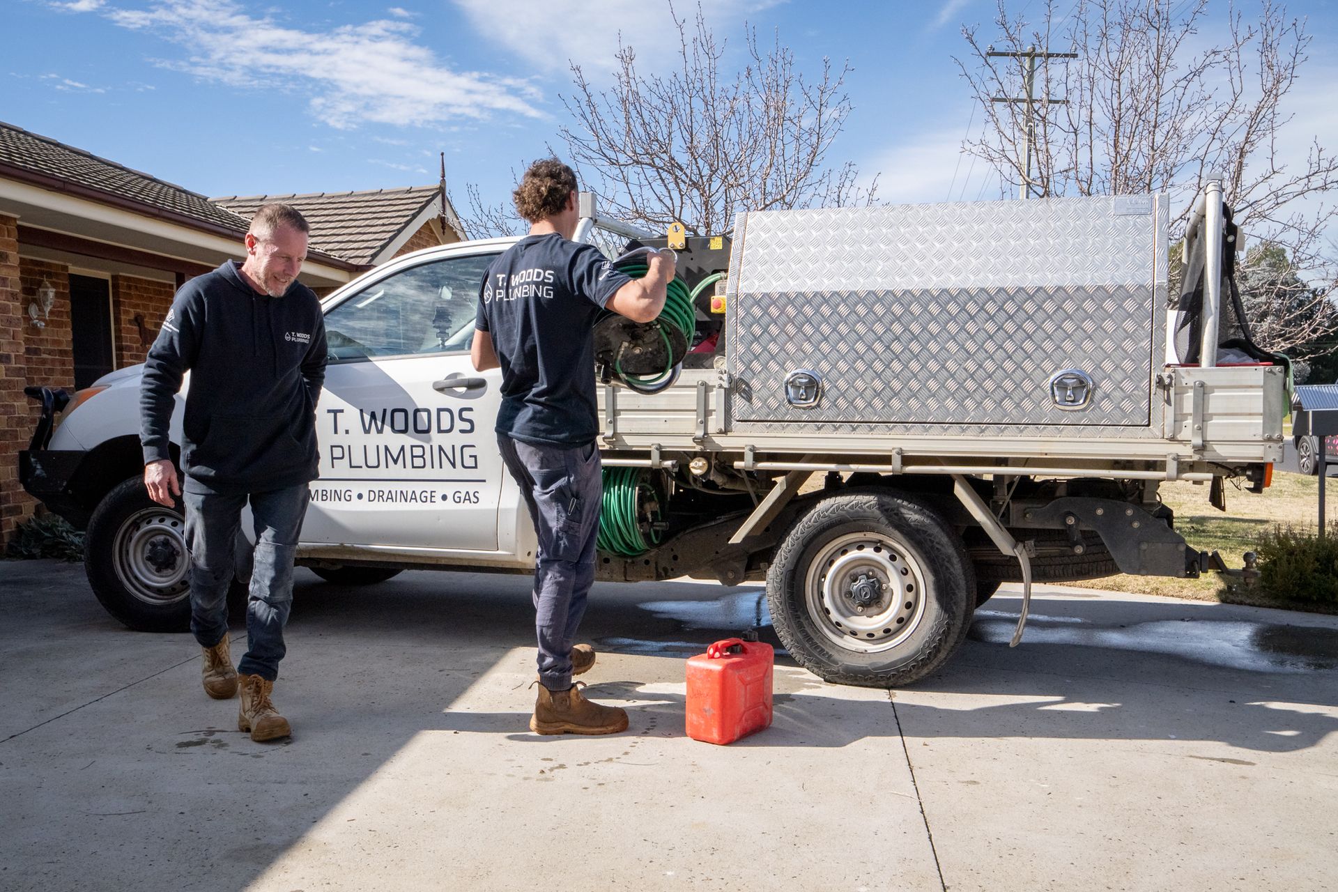 Two workers unloading a large metal container from a utility truck in a driveway — T. Woods Plumbing in Bathurst, NSW
