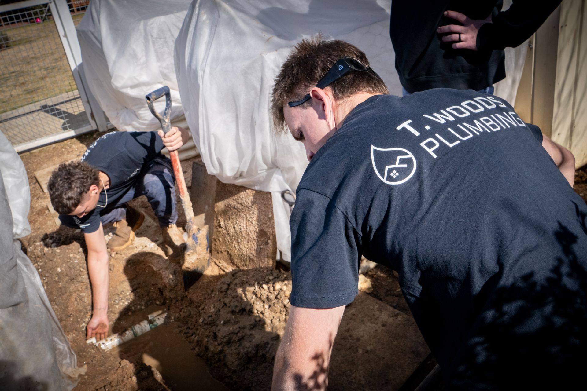 Workers digging dirt beside a white tent, one in navy shirt labeled “T. WODDS PLUMBING.” — T. Woods Plumbing in Bathurst, NSW