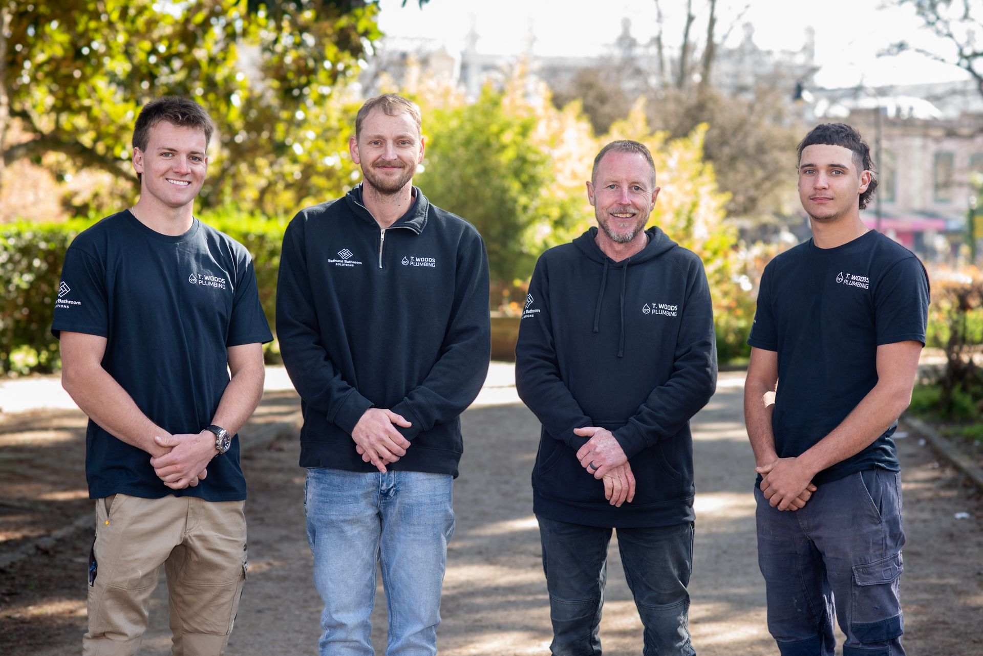 Four people in black jackets standing outdoors in a sunny park setting  — T. Woods Plumbing in Bathurst, NSW