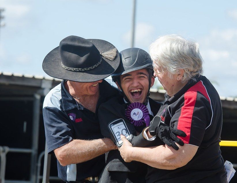 Man in helmet celebrates with supporters, holding a ribbon, smiles with excitement.