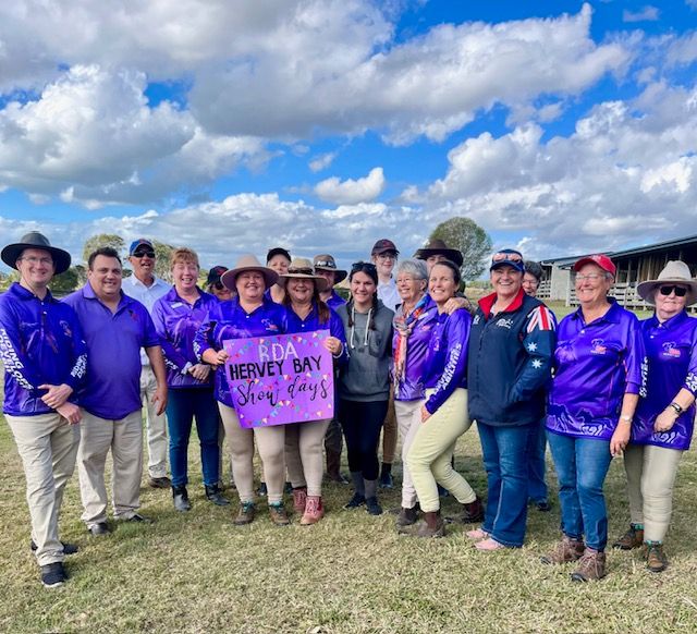 Group of people in purple shirts holding a sign that says 