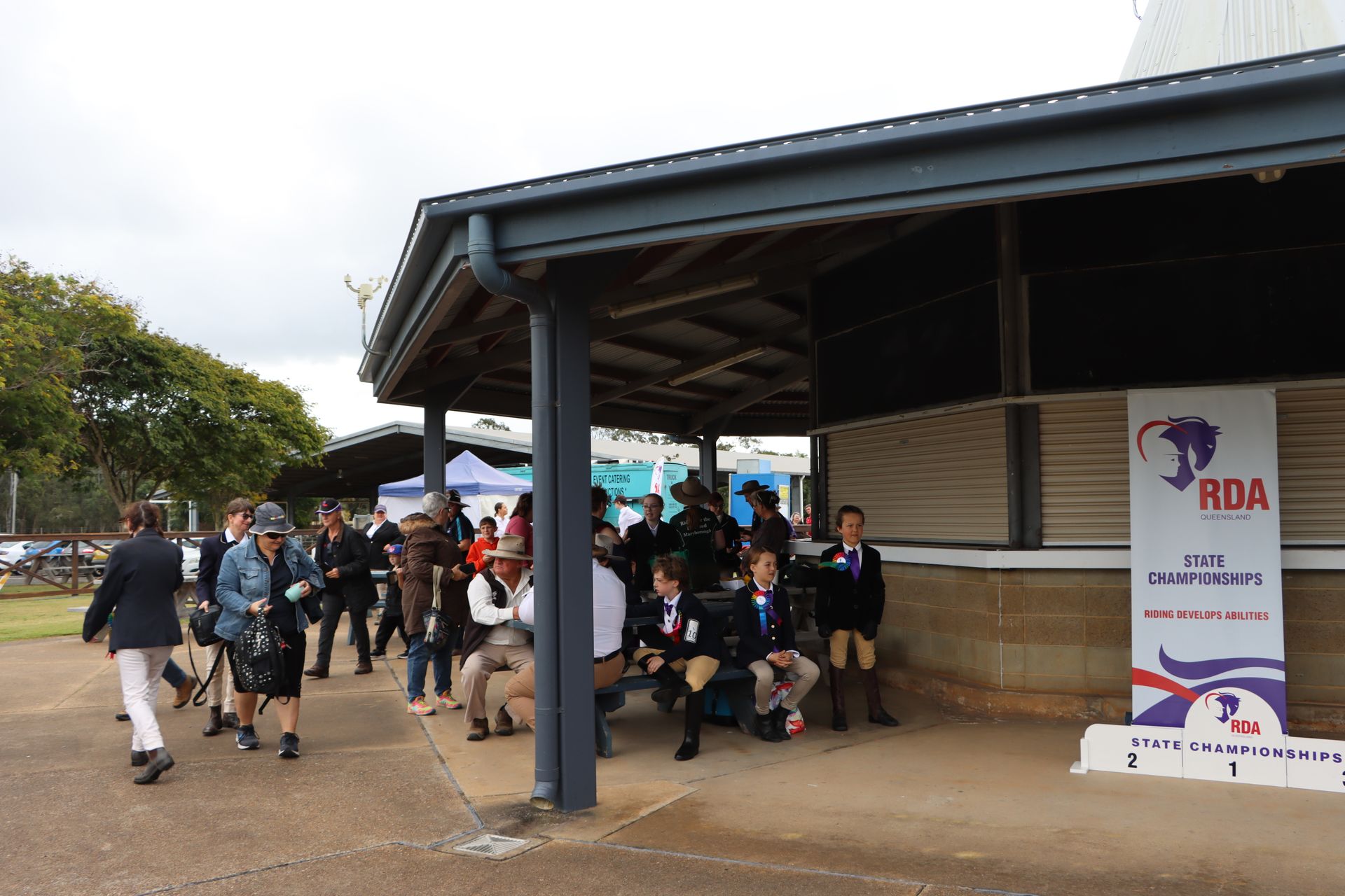 People gather at an RDA event under a shelter. A sign is visible with a logo.