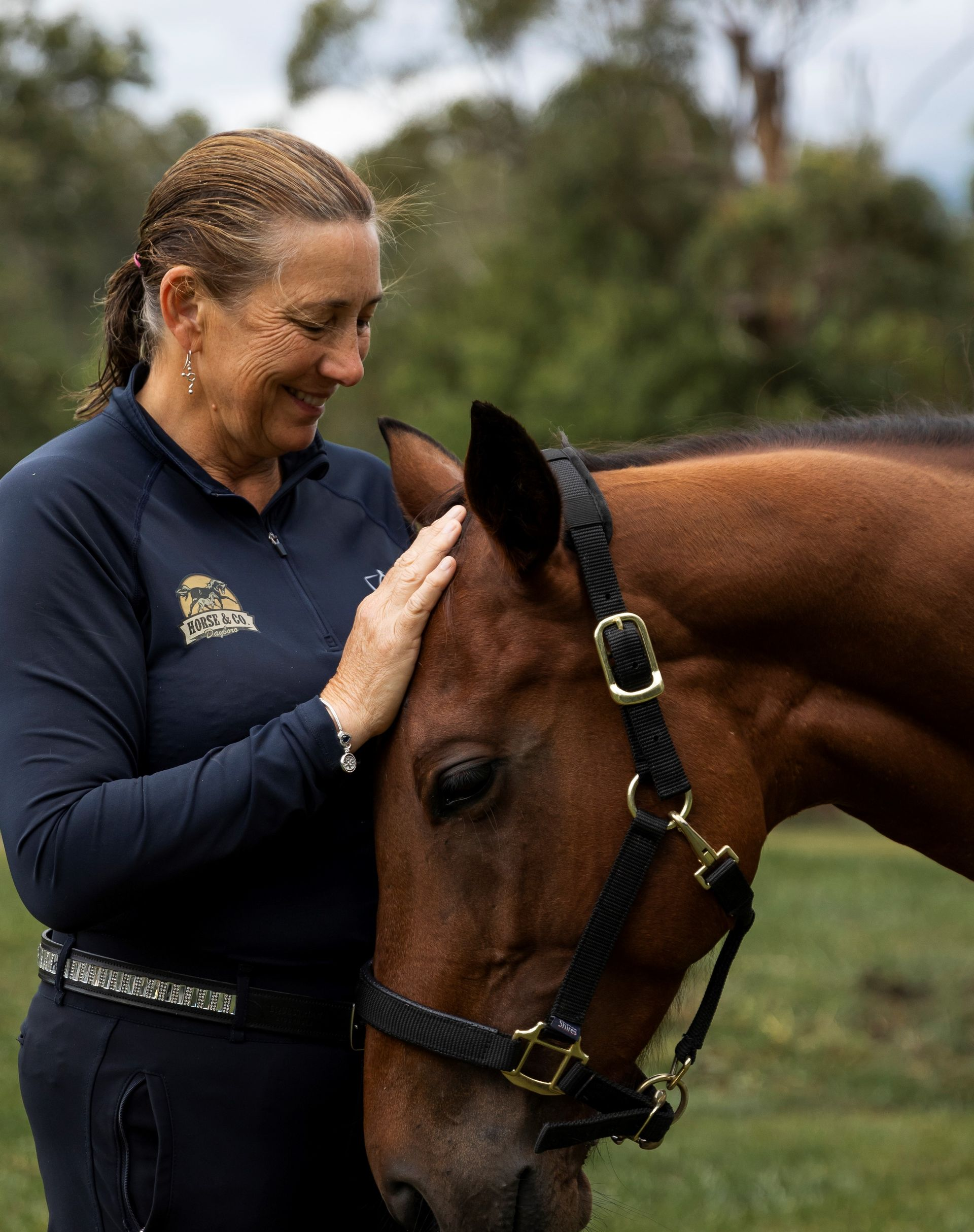 Woman with short white hair, wearing a purple polo shirt, and sunglasses on her head; outdoors.