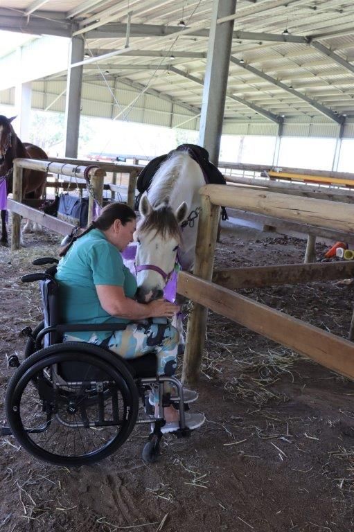 Woman in wheelchair petting a horse in an indoor stable.