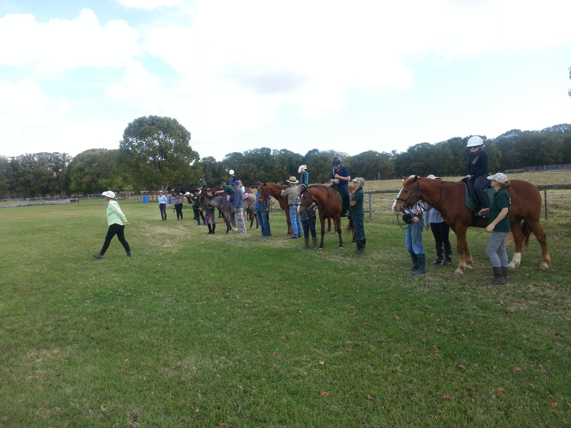People on horseback and on foot in a grassy field, near trees.