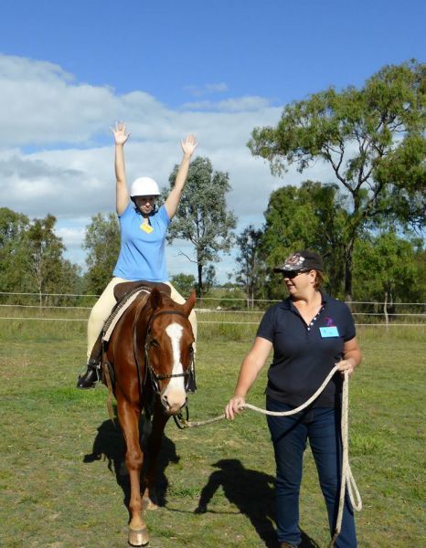 Woman on horse with arms raised, led by another woman in a grassy field on a sunny day.