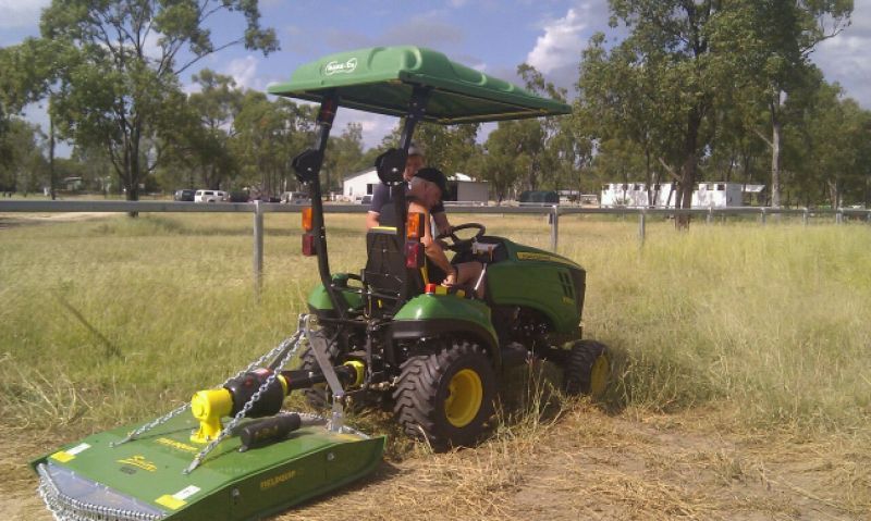 A John Deere tractor mowing tall grass in a field; person is operating the tractor.
