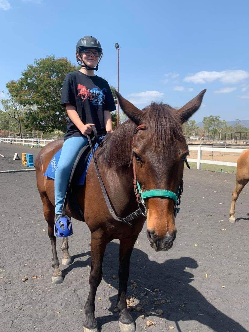 Person wearing a helmet riding a brown horse outdoors.