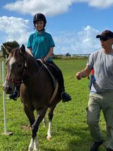 A person wearing a riding helmet on a brown horse, guided by a person in a field.