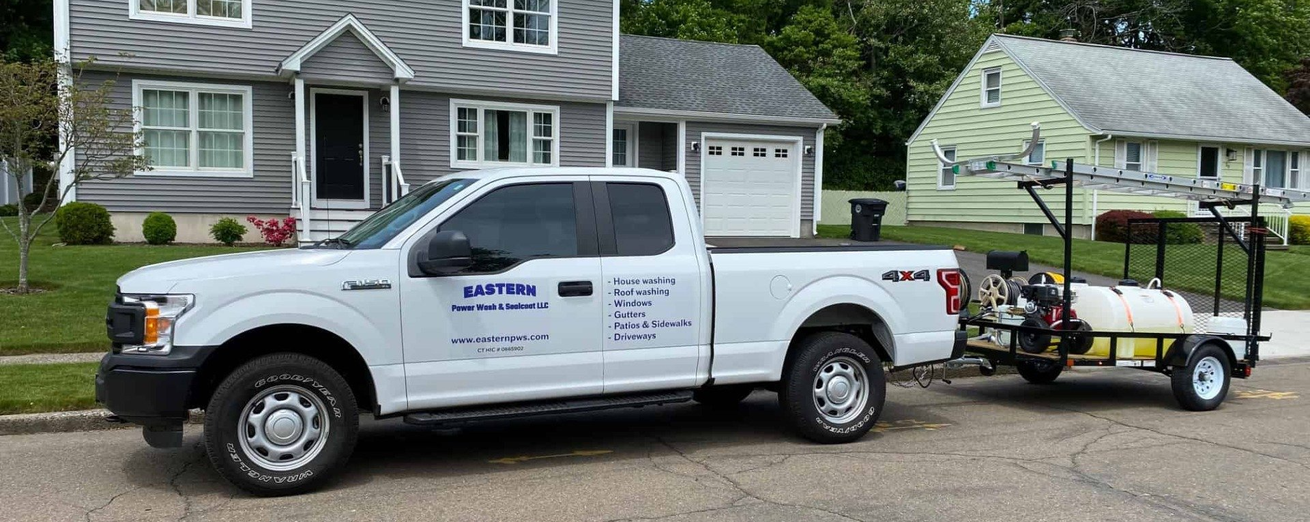 A white truck with a trailer attached to it is parked in front of a house.