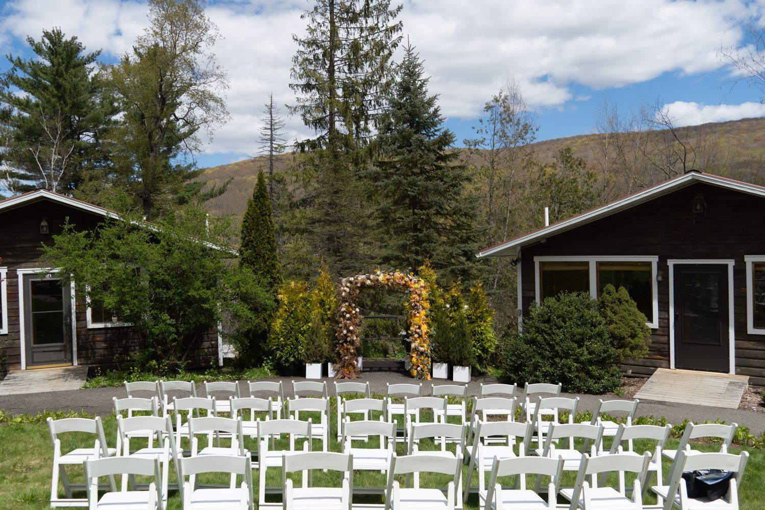 Rows of white chairs outdoors, set for a wedding. Scenic Catskill views in background and two Belleayre Lodge cabins.