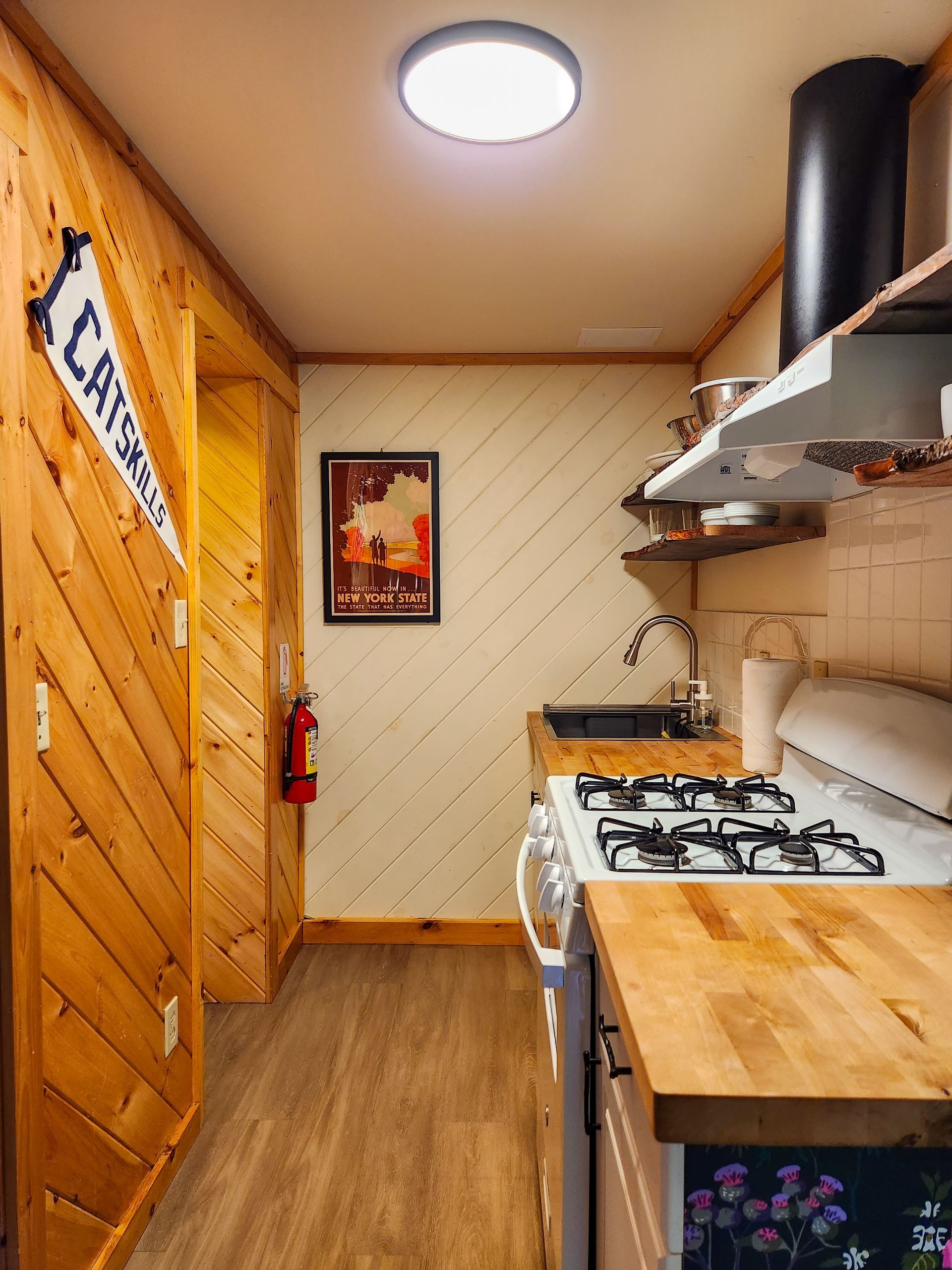 Kitchen of Cabin #4B at Belleayre Lodge in the Catskills, showing stove, sinks, stylish wall decor, and shelves.
