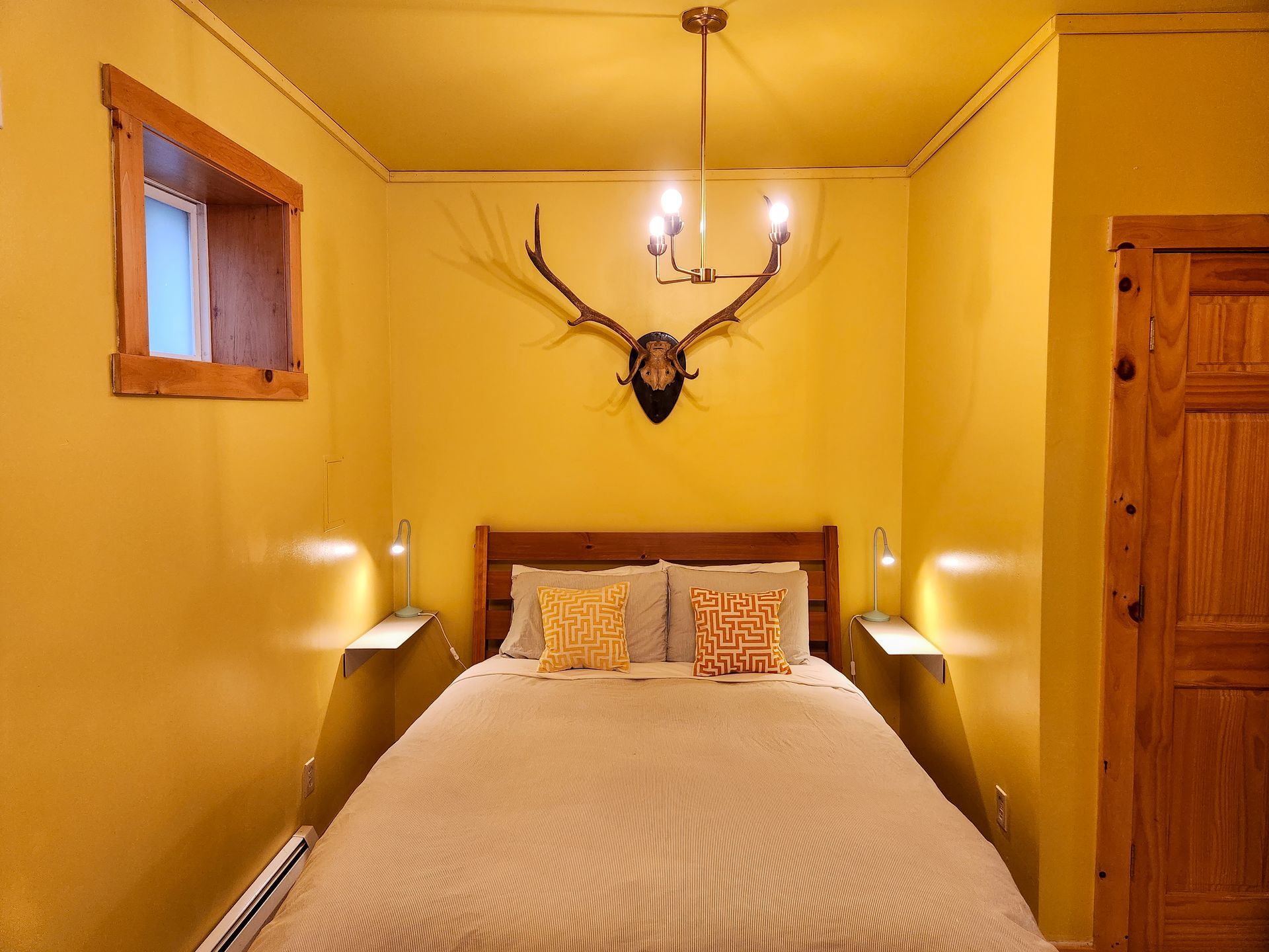 Cozy hotel-style bedroom of Cabin #7 at Belleayre Lodge, showing queen bed, stylish wall decor, and beautiful lighting.