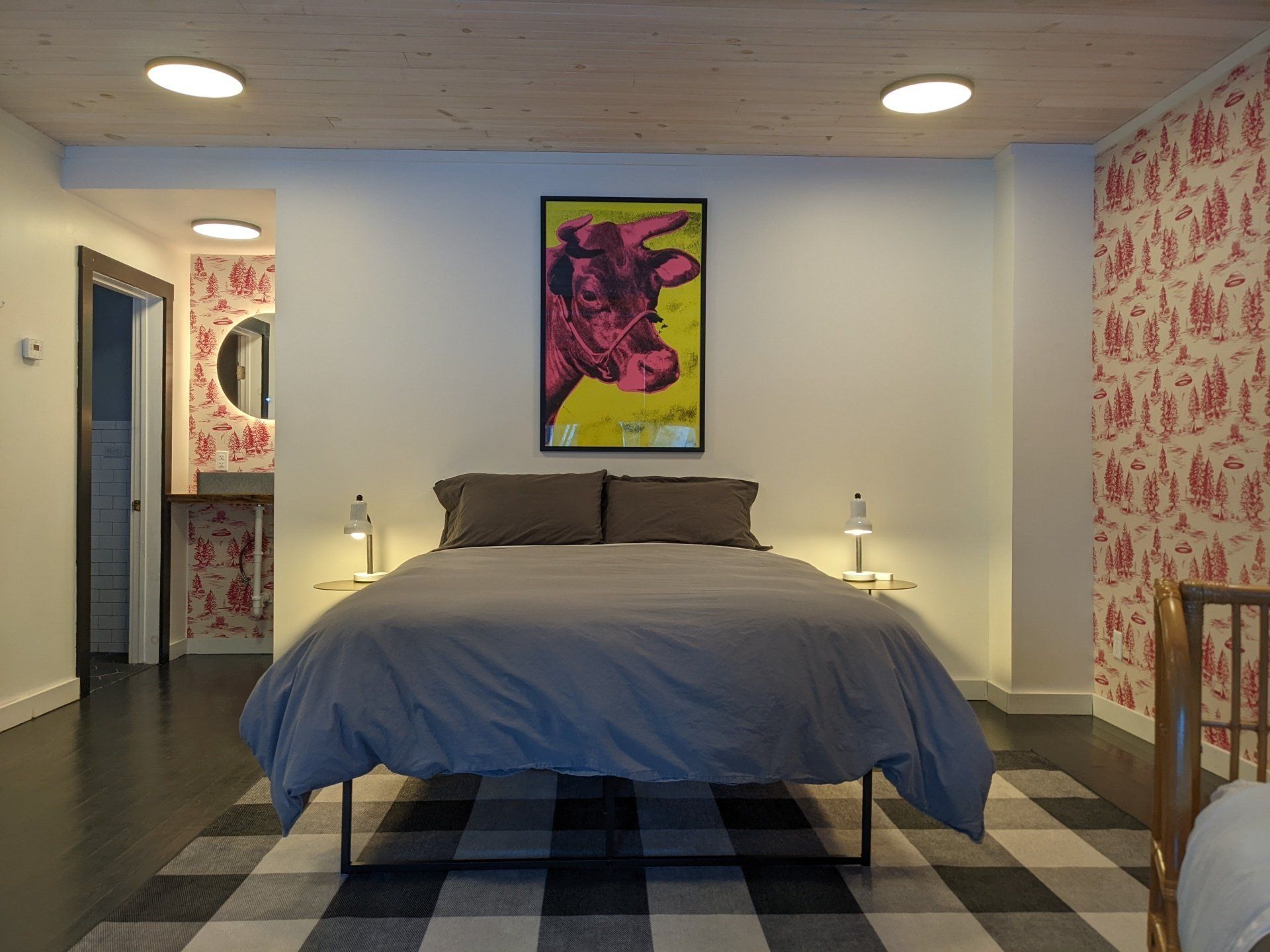 Cozy hotel-style bedroom of Cabin #227 at Belleayre Lodge, showing queen bed, decorative art, and bedside lamps.