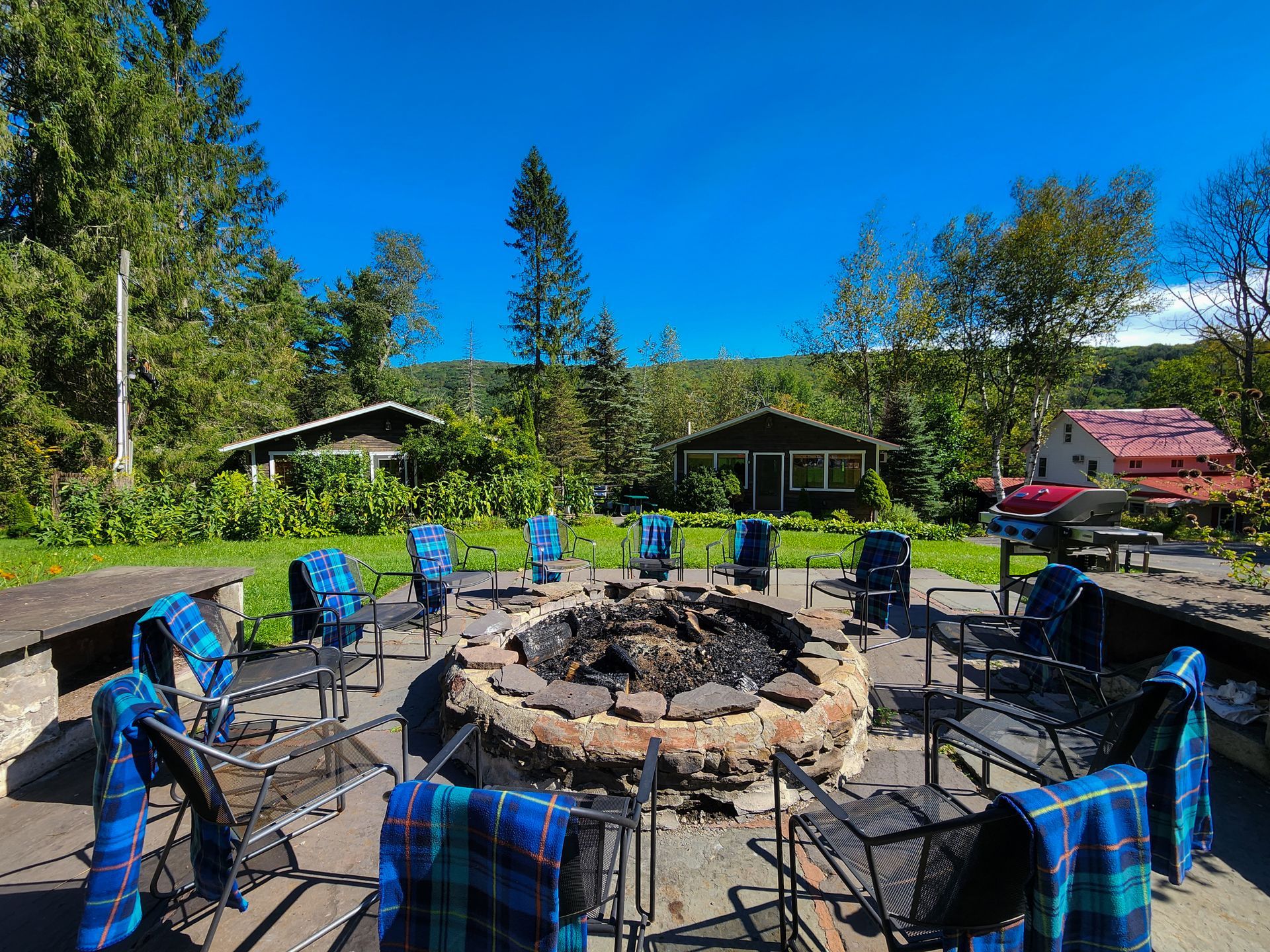 Outdoor photo of Belleayre Lodge's cozy stone fire pit, surrounded by chairs. Scenic Catskills views in the background.