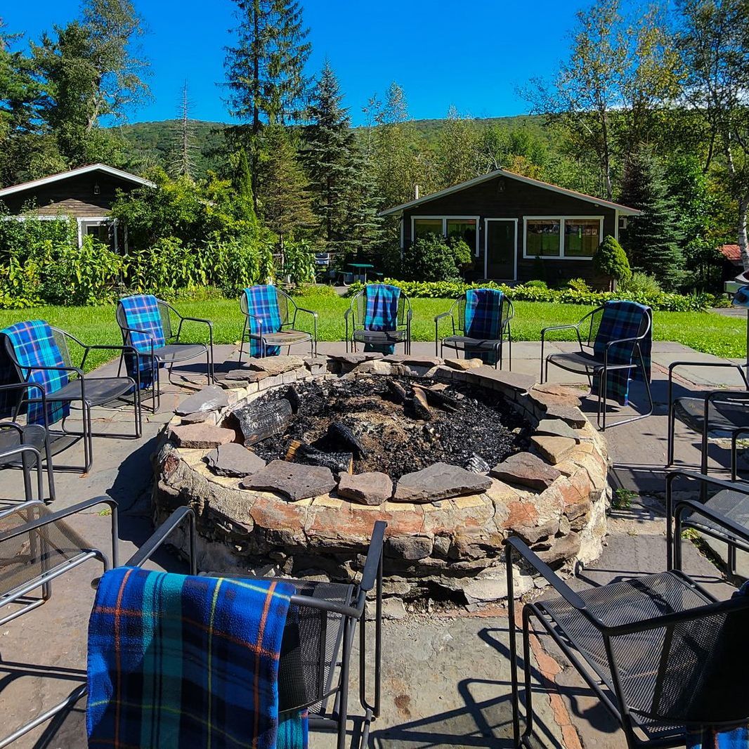 Outdoor photo of Belleayre Lodge's cozy stone fire pit, surrounded by chairs. Scenic Catskills views in the background.