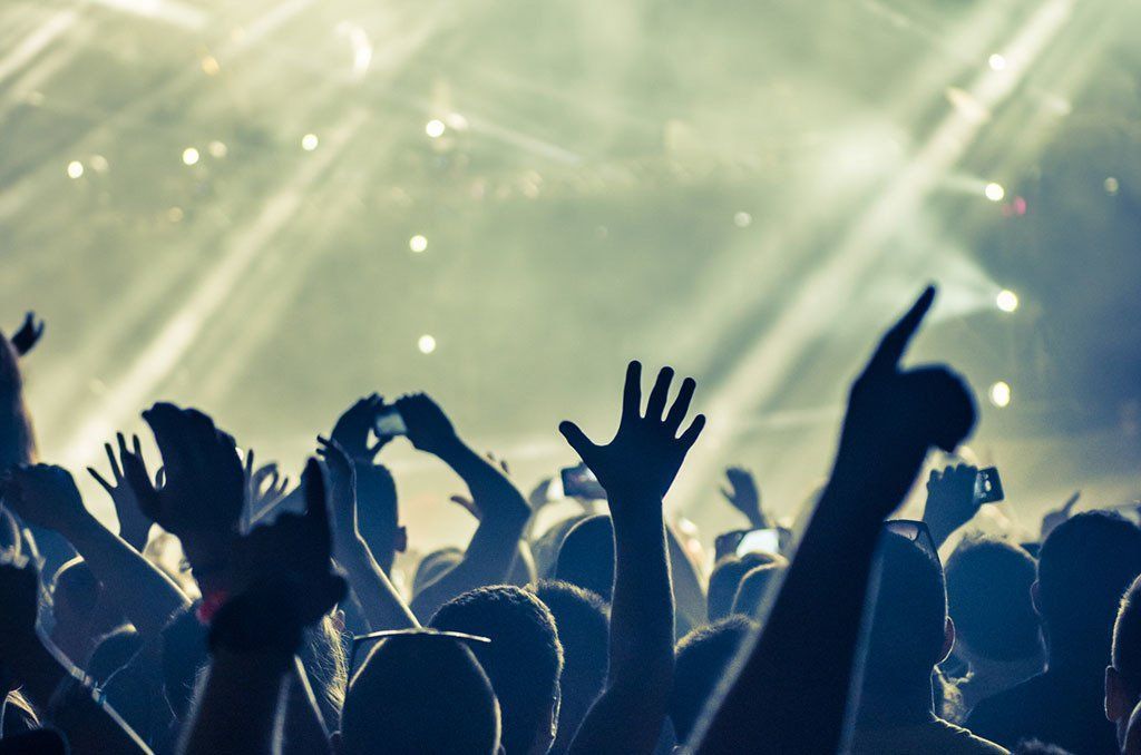 A crowd of people are raising their hands in the air at a concert.