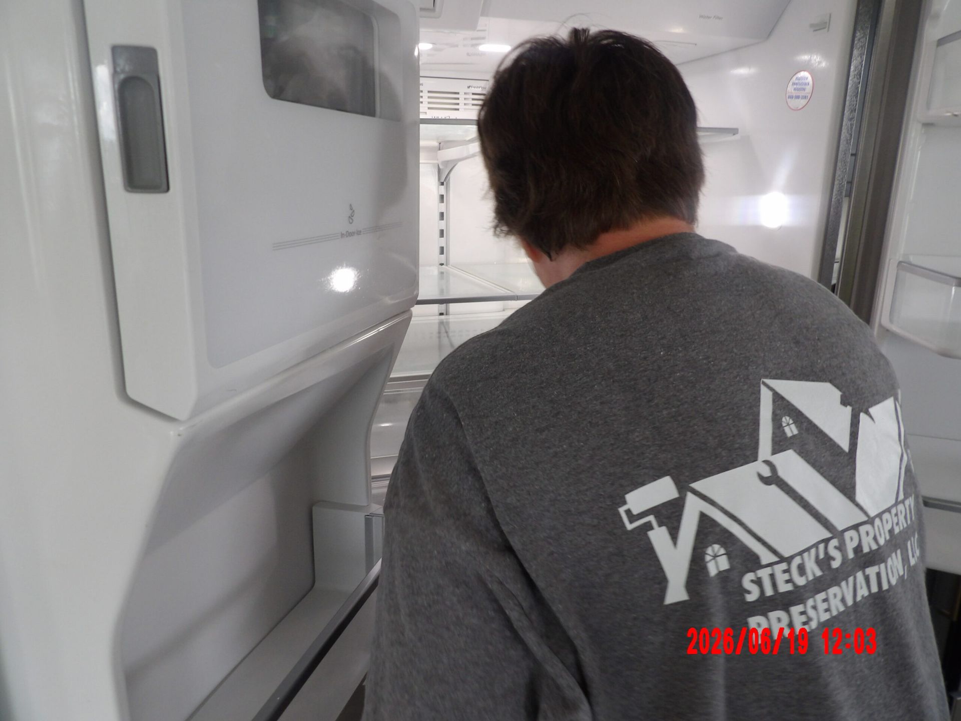 Person in a gray shirt leaning into a white industrial enclosure or cabinet, viewed from behind.