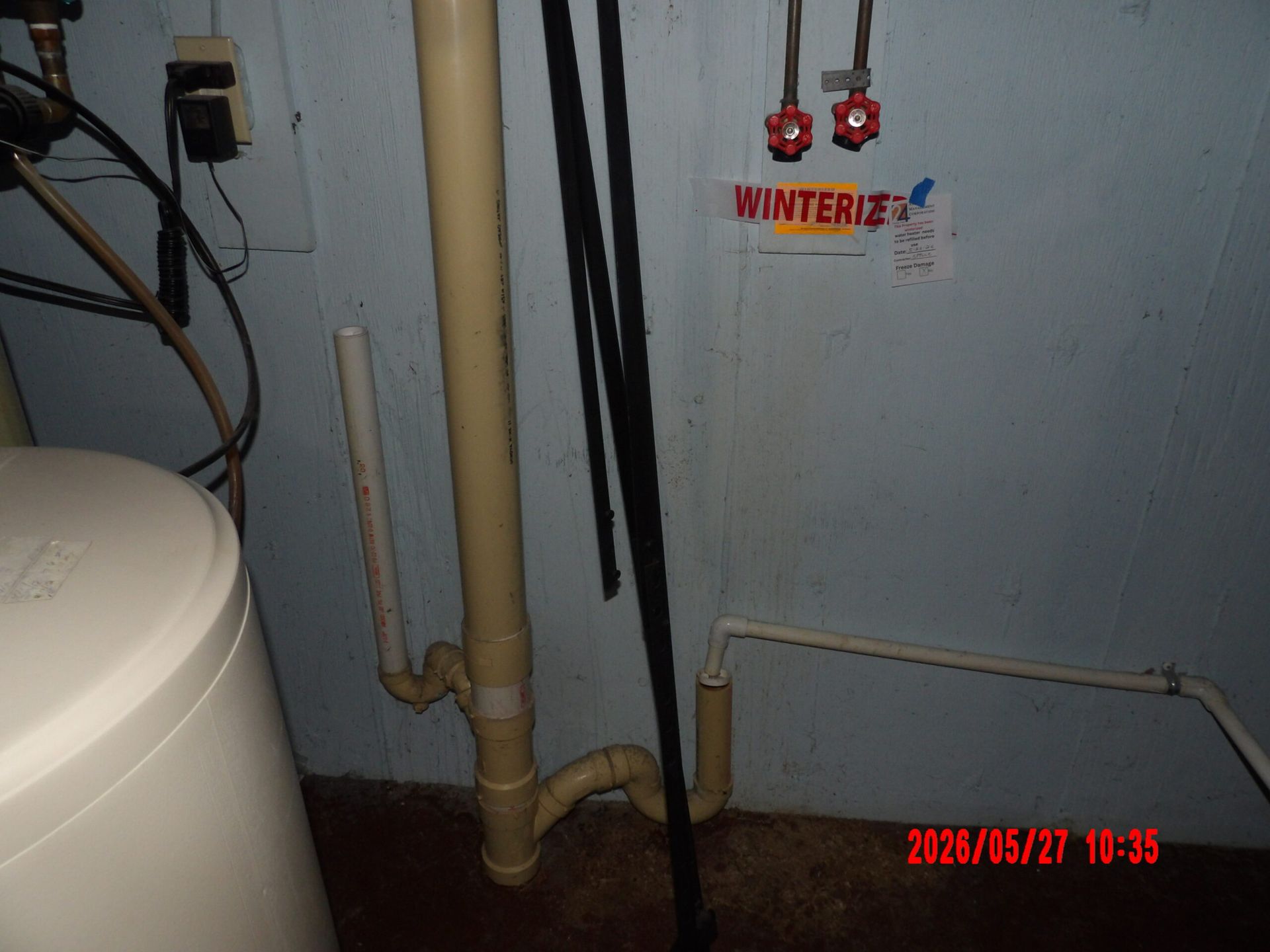 Basement utility area with pipes, water heater, and wall-mounted valves near a concrete wall.