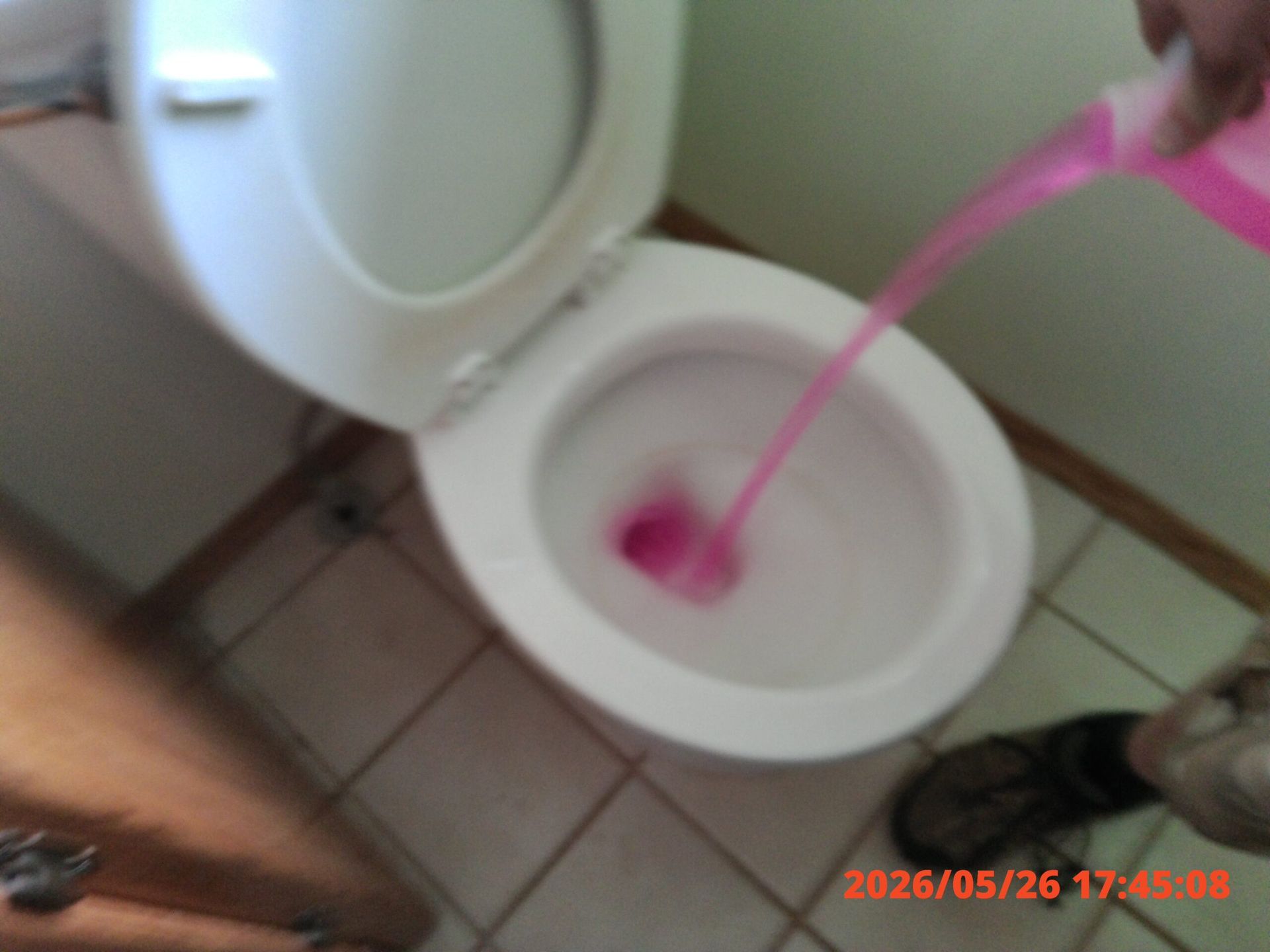 Pink liquid being poured into a toilet bowl in a bathroom.
