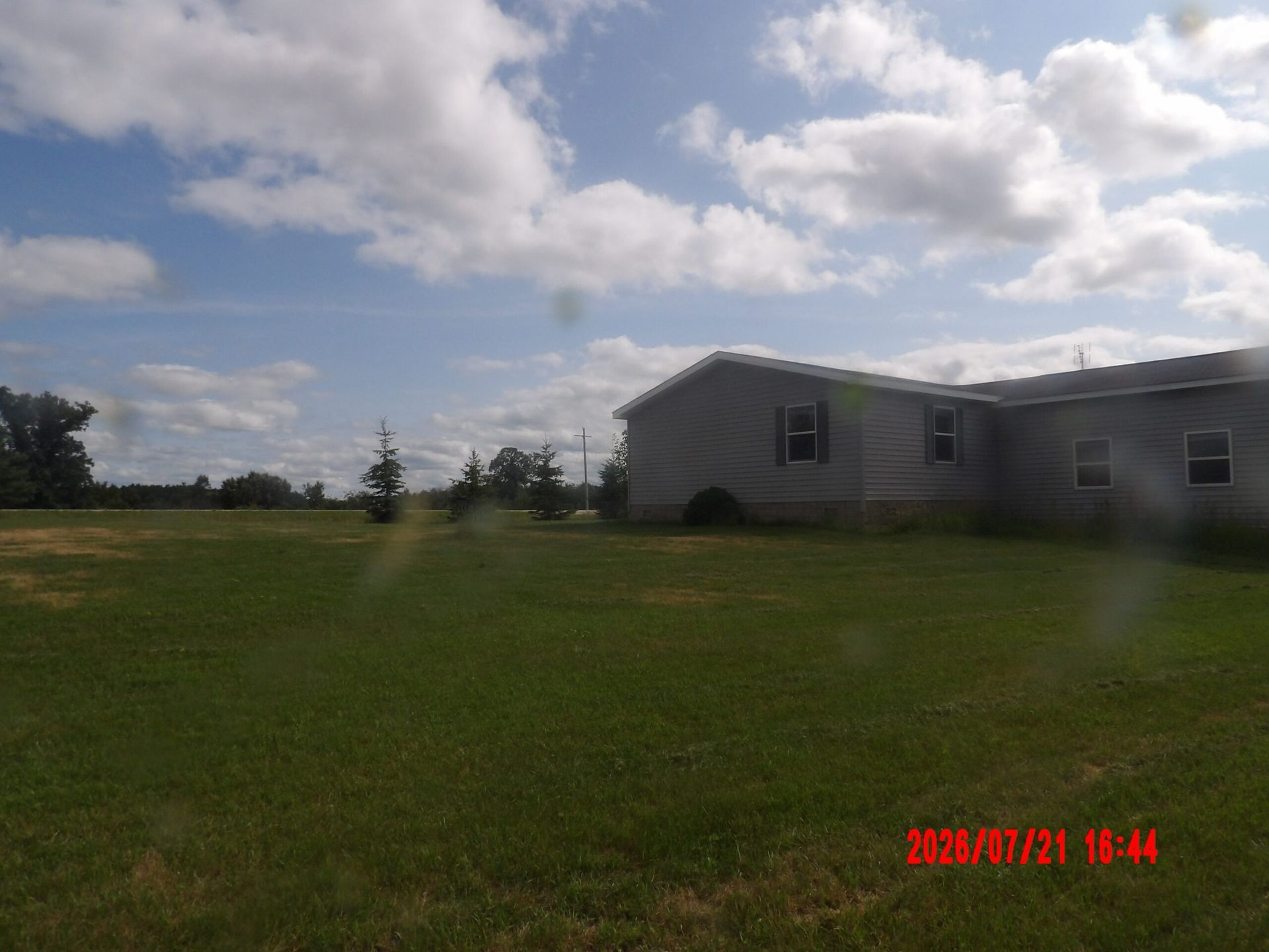 Large grassy yard beside a gray house under a cloudy blue sky