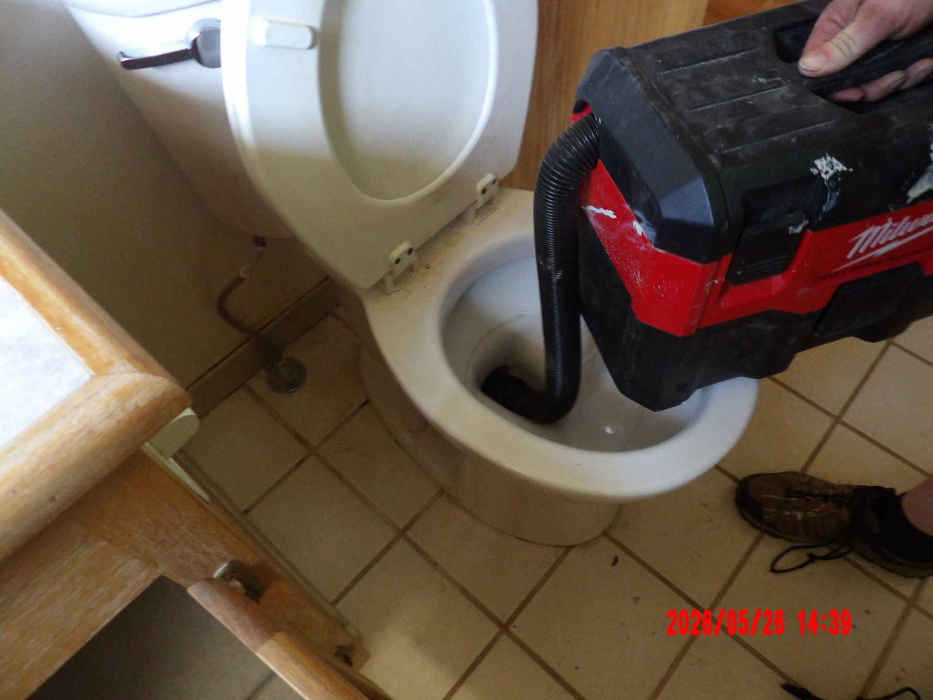 Red-and-black shop vac hose inserted into a white toilet bowl in a tiled bathroom