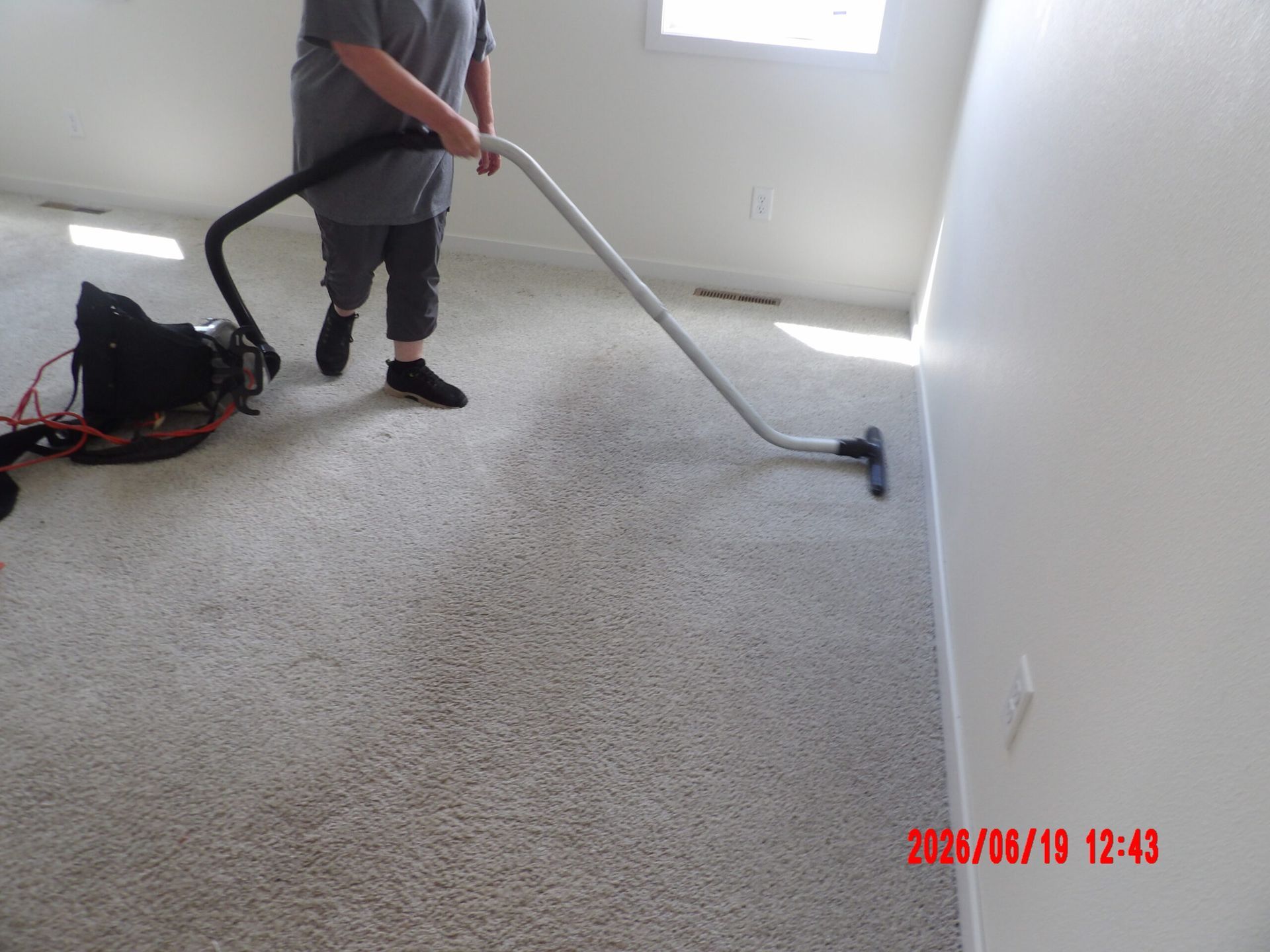 Person vacuuming a carpeted room with a canister vacuum and long hose