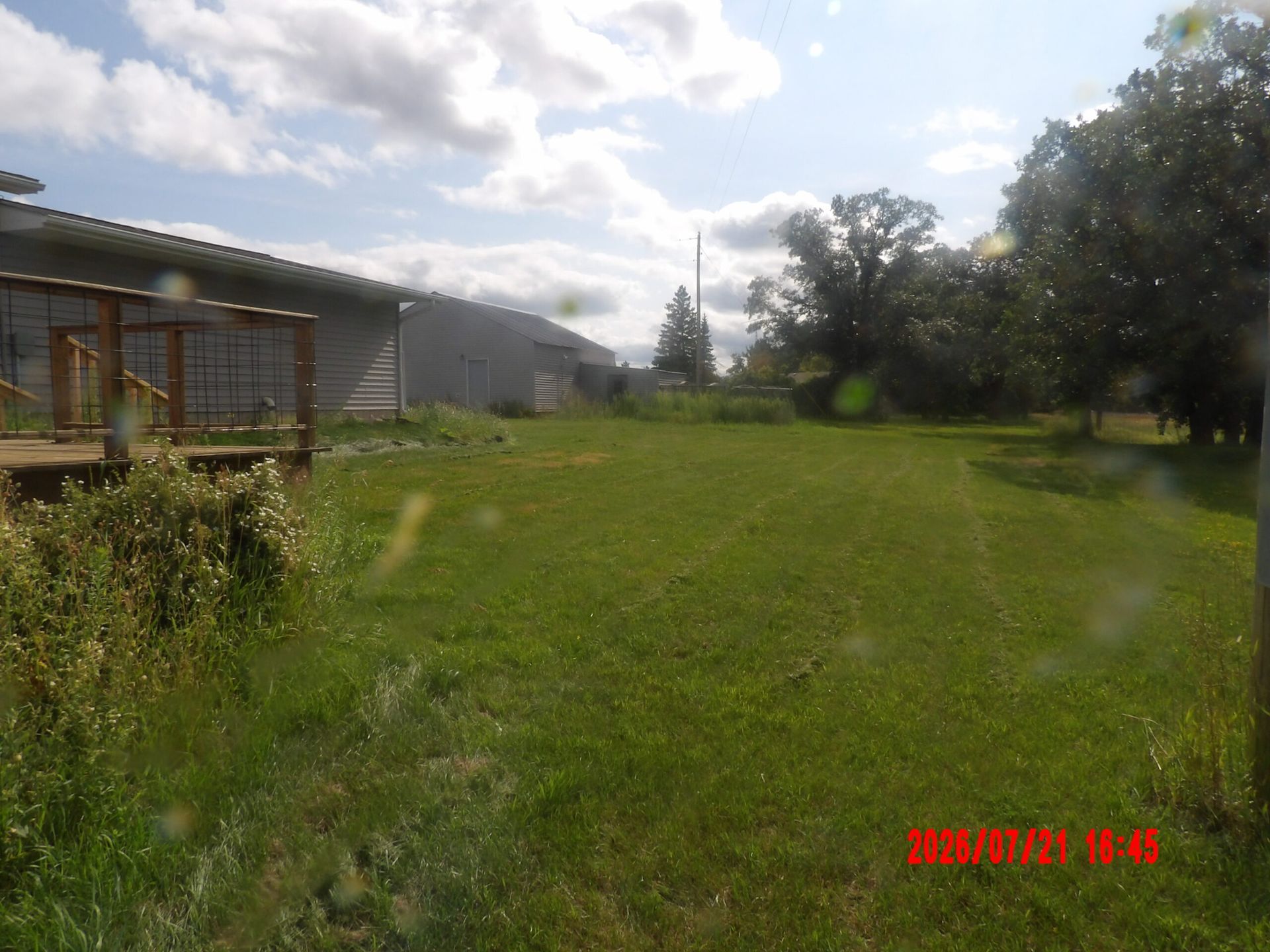 Grassy yard beside a building with trees under a cloudy sky, with a red date stamp in the corner