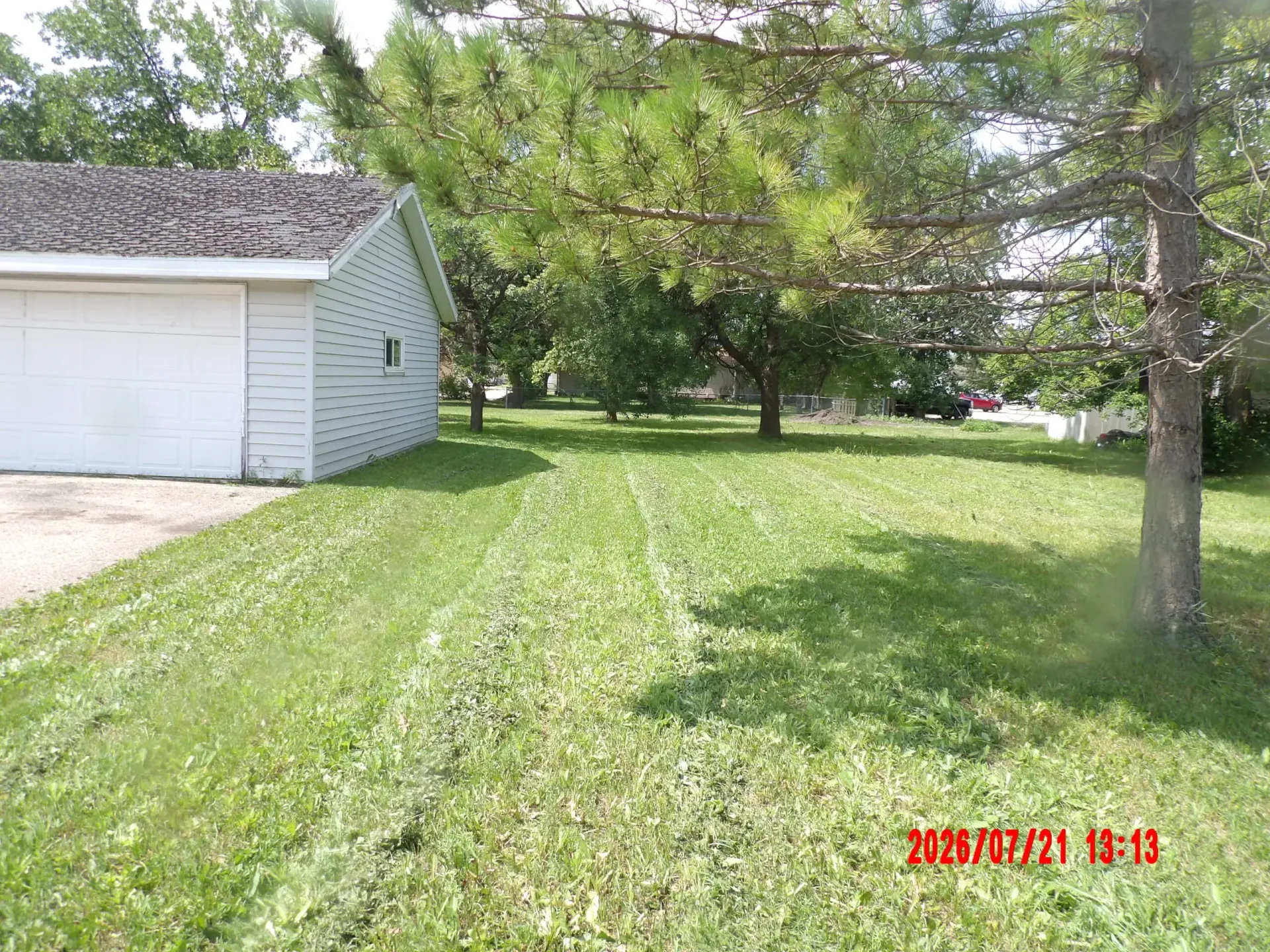 Grassy backyard beside a white garage and trees on a sunny day