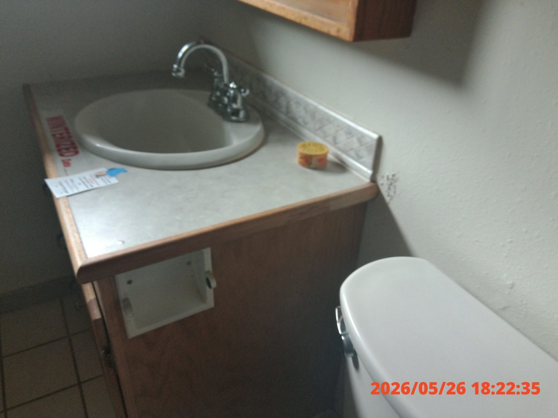 Small bathroom vanity with white sink, chrome faucet, and toilet beside tiled floor.
