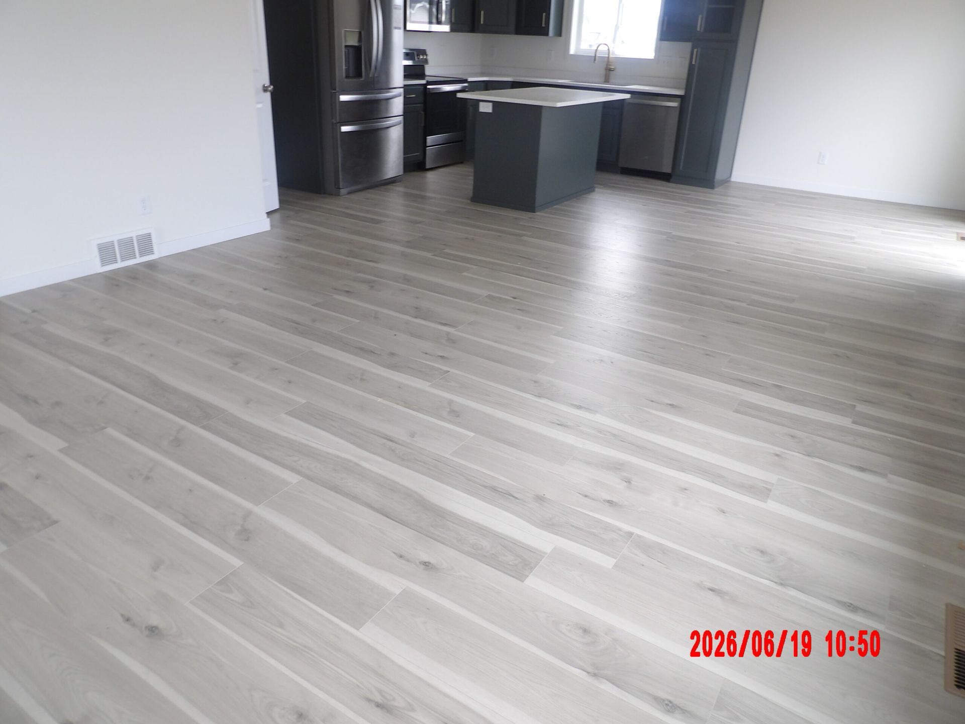 Empty modern kitchen and living area with light wood floors and gray island countertop.