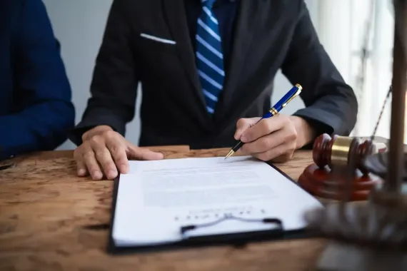 Person in a suit signing documents at a desk with a gavel