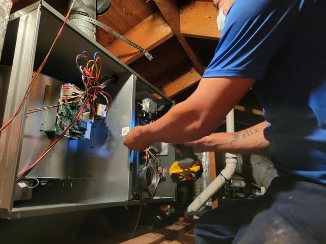 Technician wiring an HVAC unit in a basement with exposed ducts and tools nearby