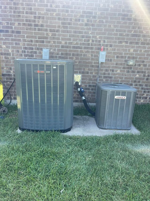 Two outdoor air conditioning units against a brick wall beside a patch of grass