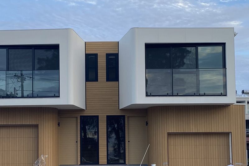 A modern duplex featuring two white box-like upper levels, dark windows, and light wood-paneled walls above two garages.