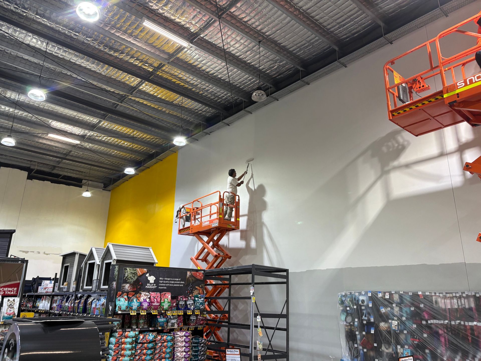 A white van parked under a large warehouse awning next to orange construction barriers and a yellow safety railing.