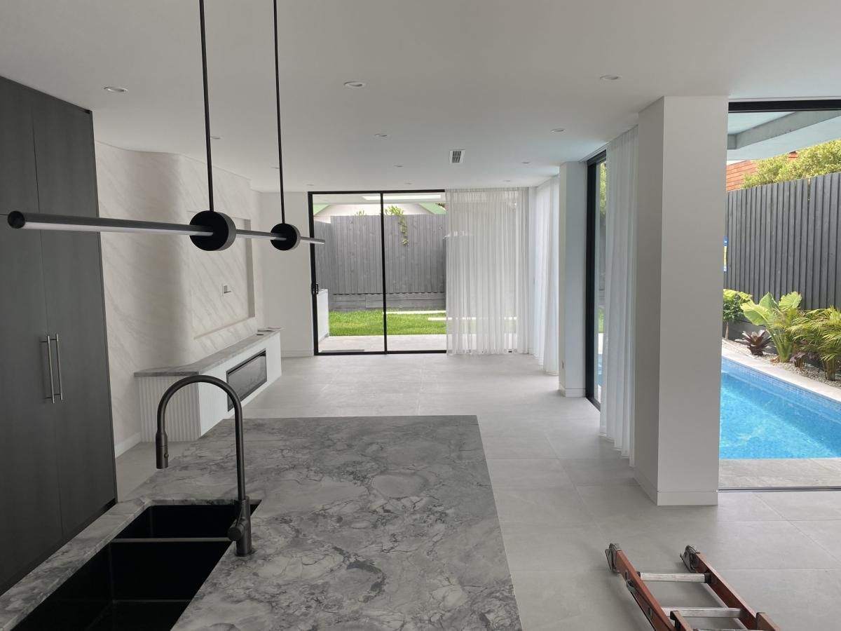 Modern kitchen interior with a stone island and sink, opening to a living area with large windows and a swimming pool.
