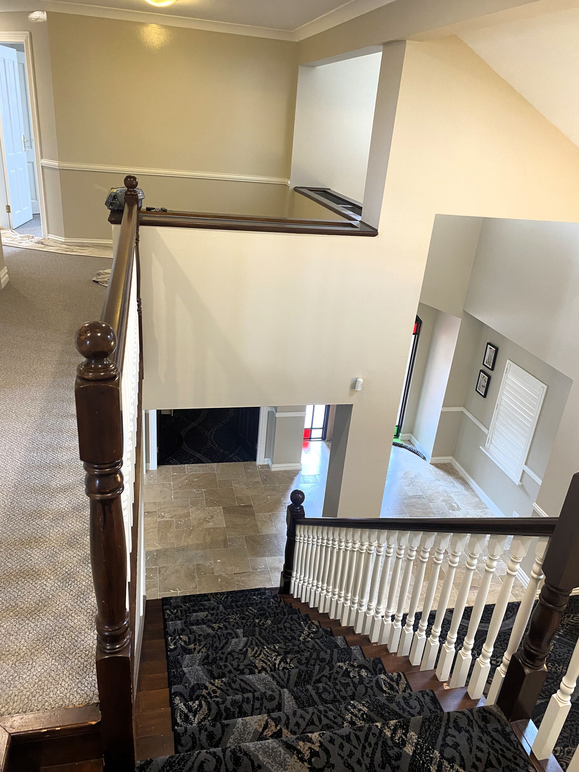 An overhead view of an indoor staircase with patterned carpet, white railings, and dark wood posts leading to a foyer.