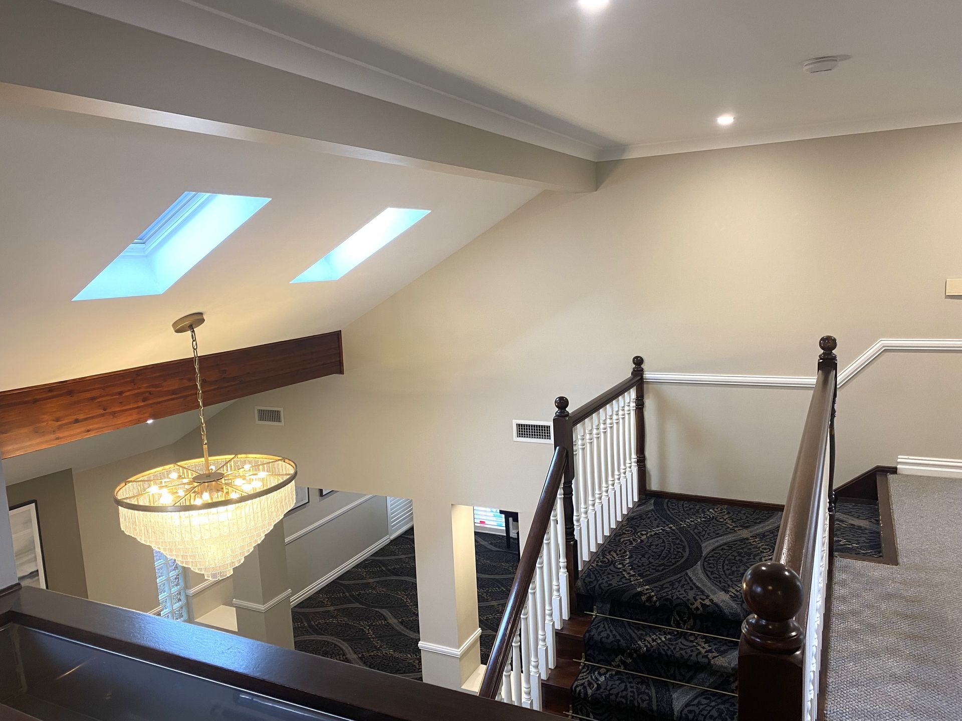 A staircase with dark patterned carpet and wooden railings leads down from a landing under a sloped ceiling with skylights.