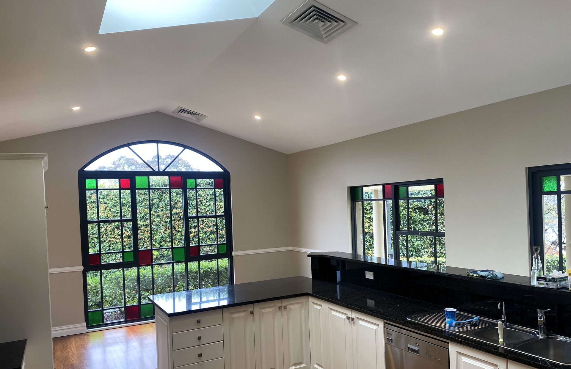 A kitchen with vaulted ceilings, recessed lighting, white cabinets, a black granite countertop, and arched stained glass.