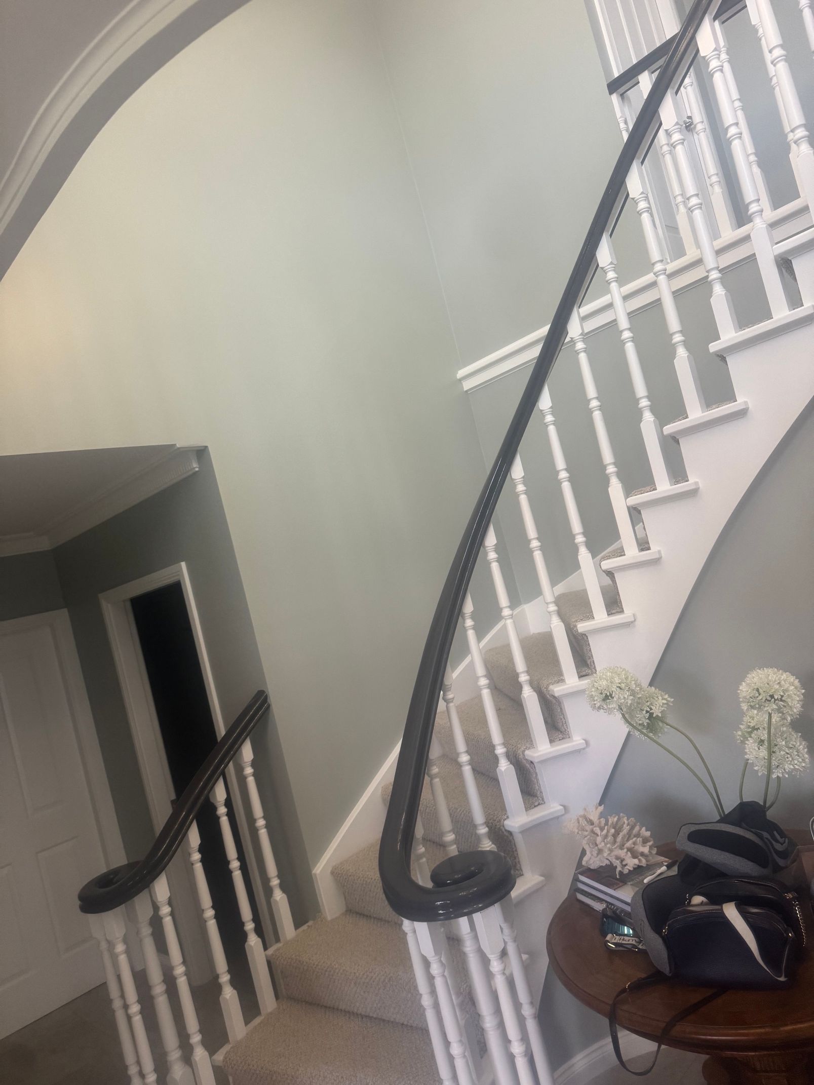 Curved staircase with black railing in a beige foyer, with a small table and flowers nearby