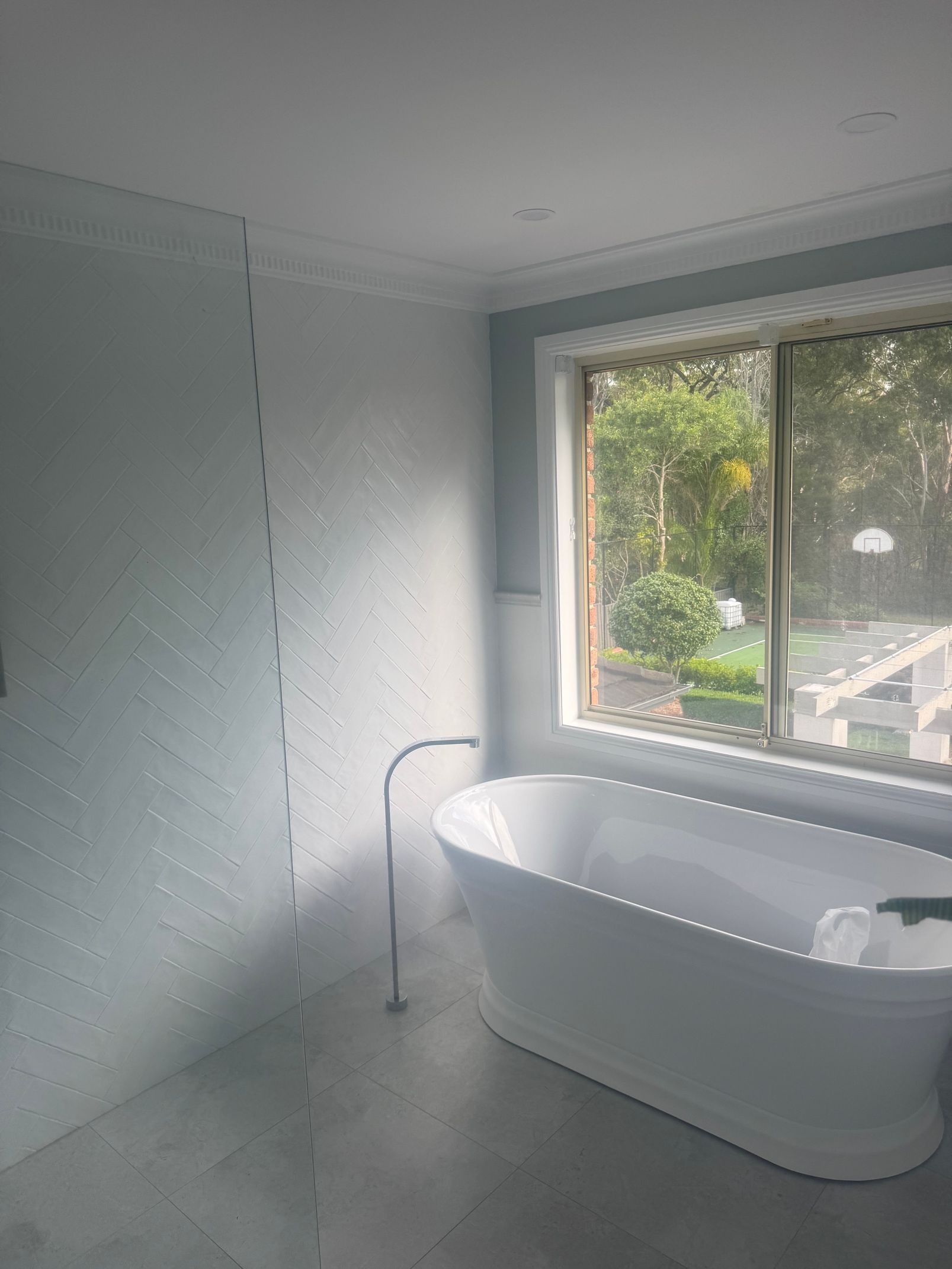 Modern white bathroom with a freestanding tub beside a large window and light gray walls
