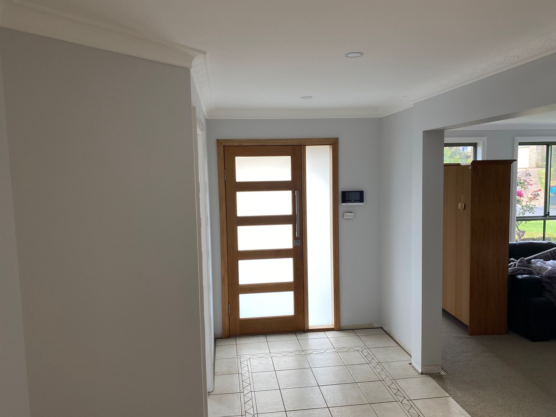 Entryway with a light-colored tiled floor, a wooden front door with horizontal frosted glass panels, and off-white walls.