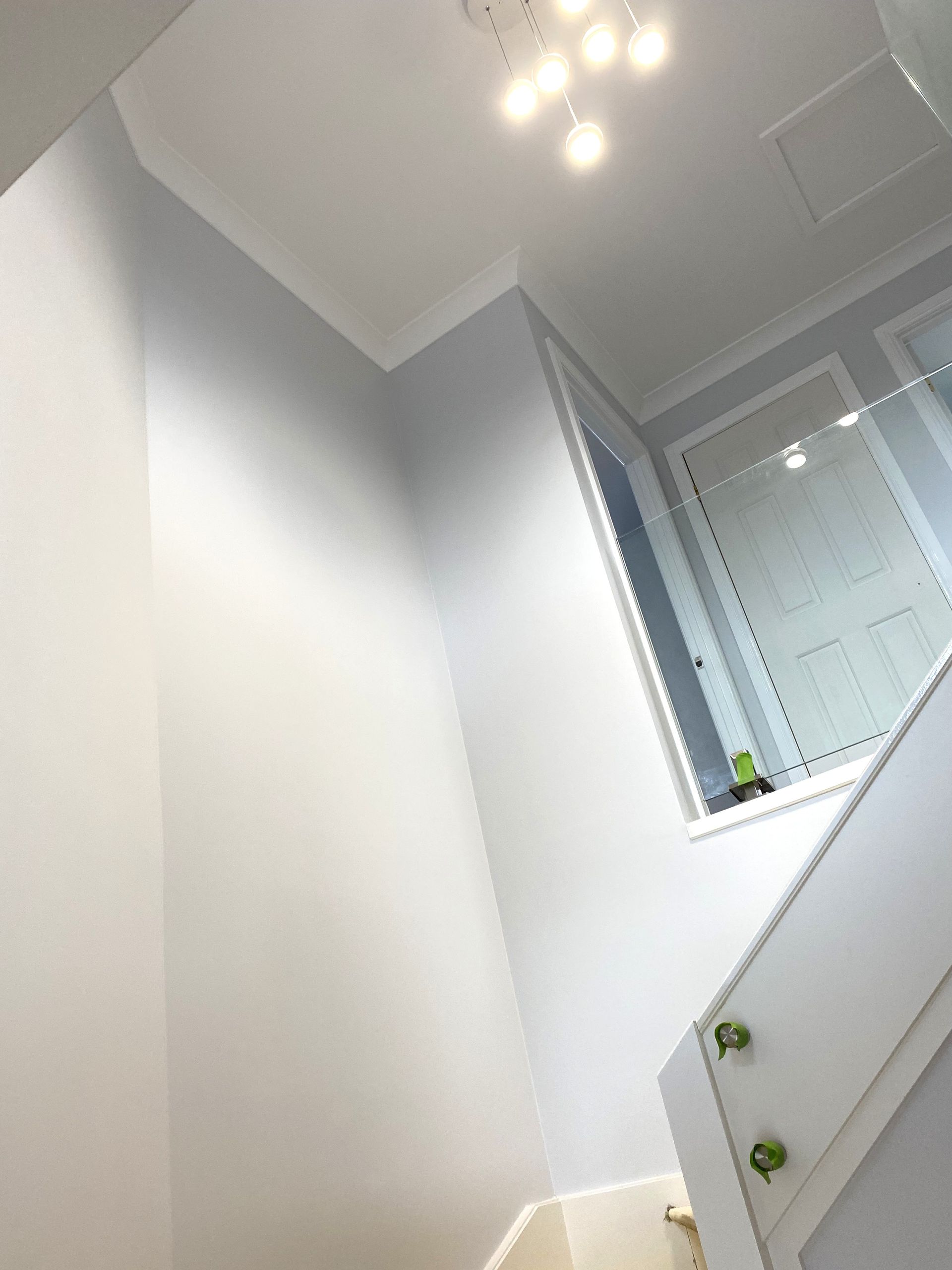 Low-angle view of a bright hallway with light grey walls, white trim, a modern ceiling light, and a wooden staircase.