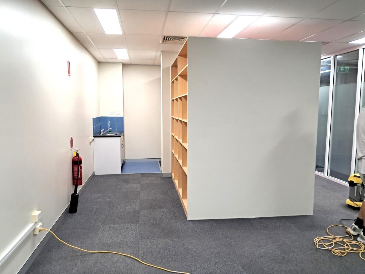 An office space featuring a large white partition wall, a corner kitchenette, and a fire extinguisher on the wall.