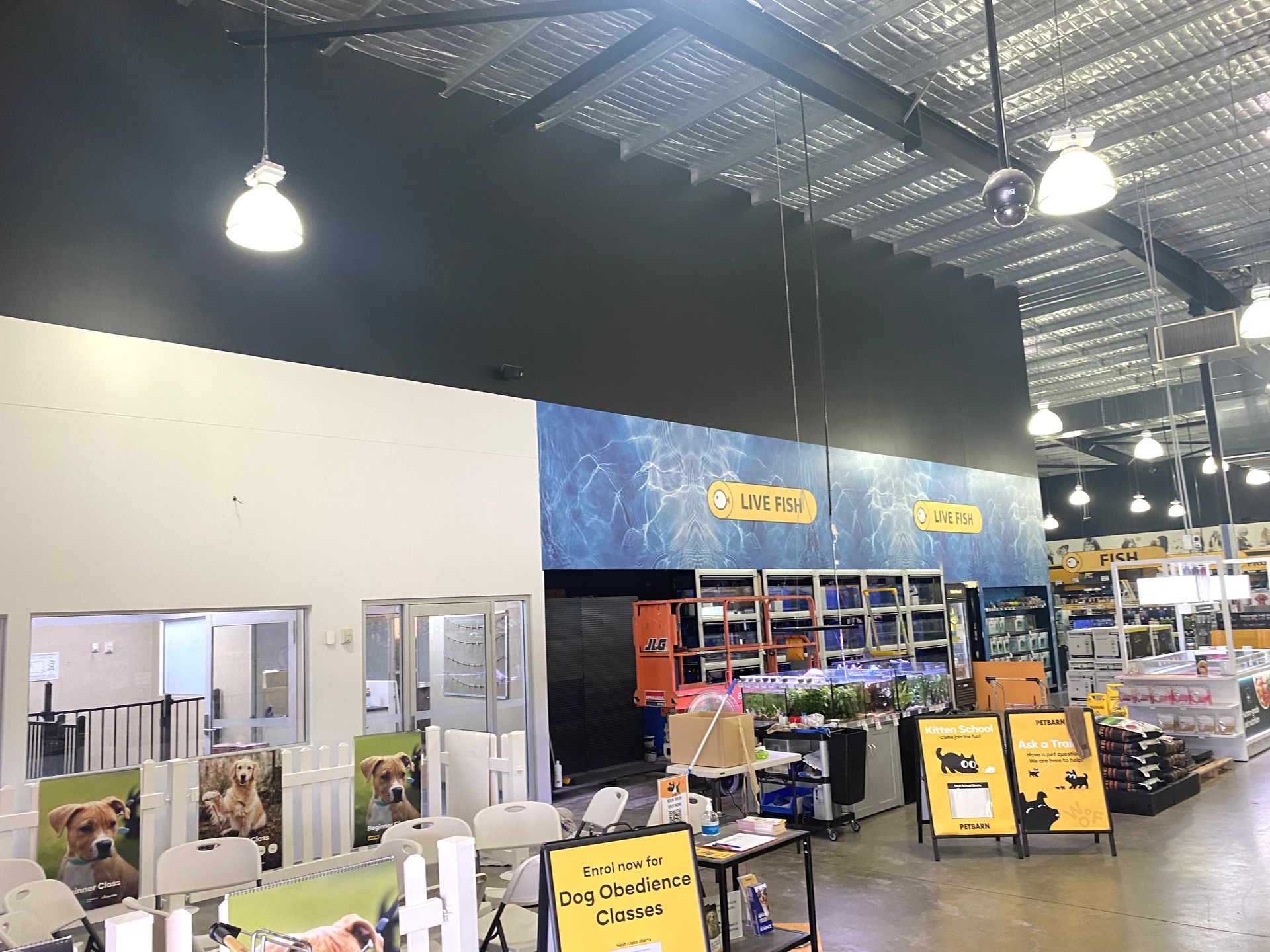 Interior view of a brightly lit pet store with product displays, hanging lights, and signage against a dark wall.