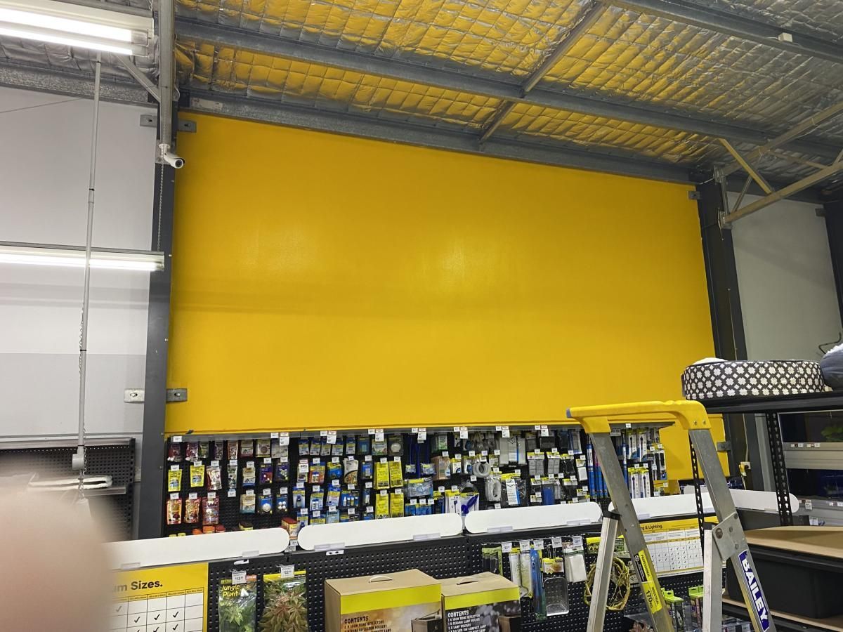 A large yellow wall panel hangs above retail shelving stocked with products in a warehouse or store.